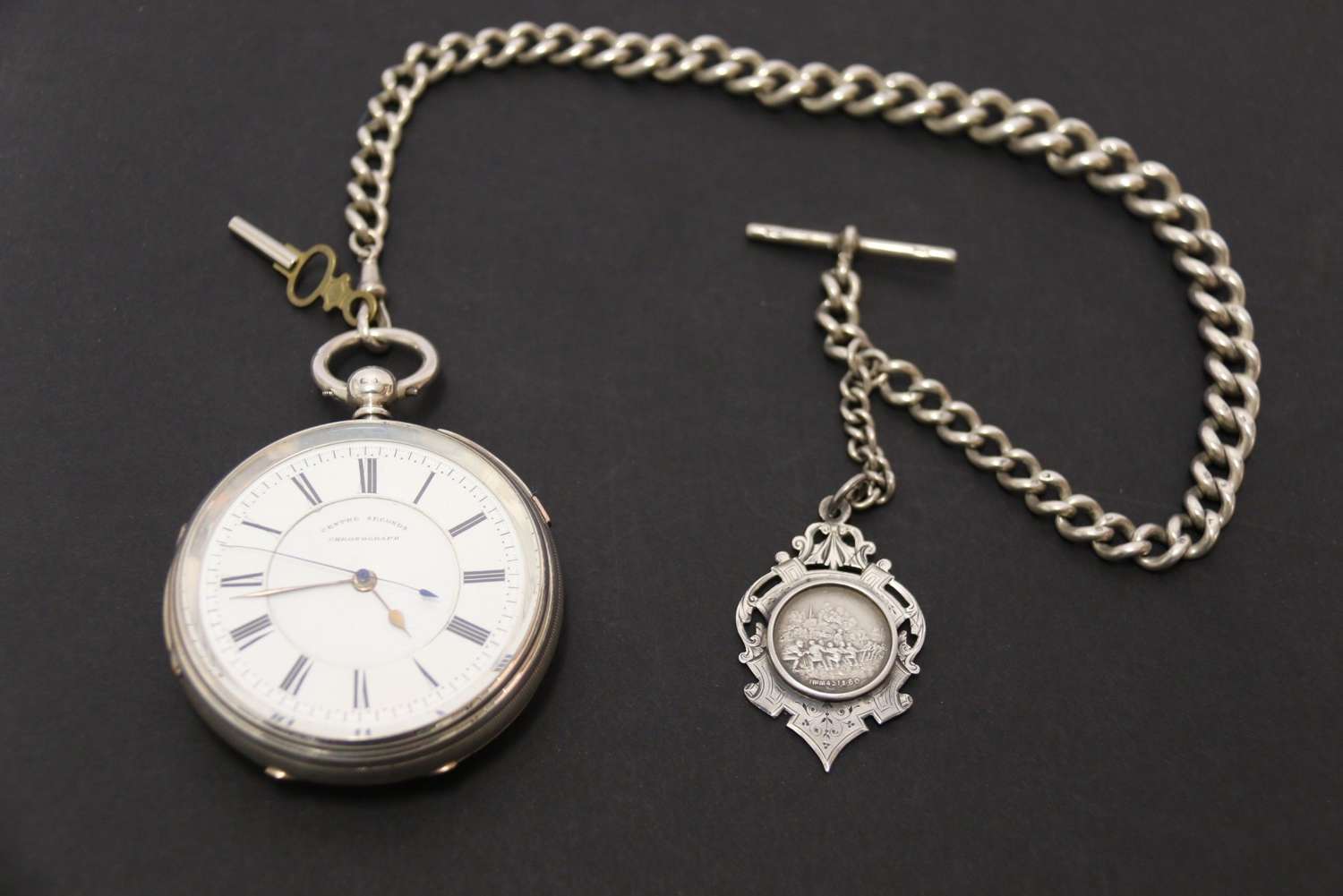 An Over Sized Silver Chronograph Pocket Watch And Chain With Mining Tug Of War Fob.