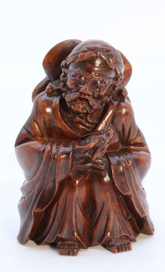 A mid 19th century Japanese Okimono of a seated man holding a bat