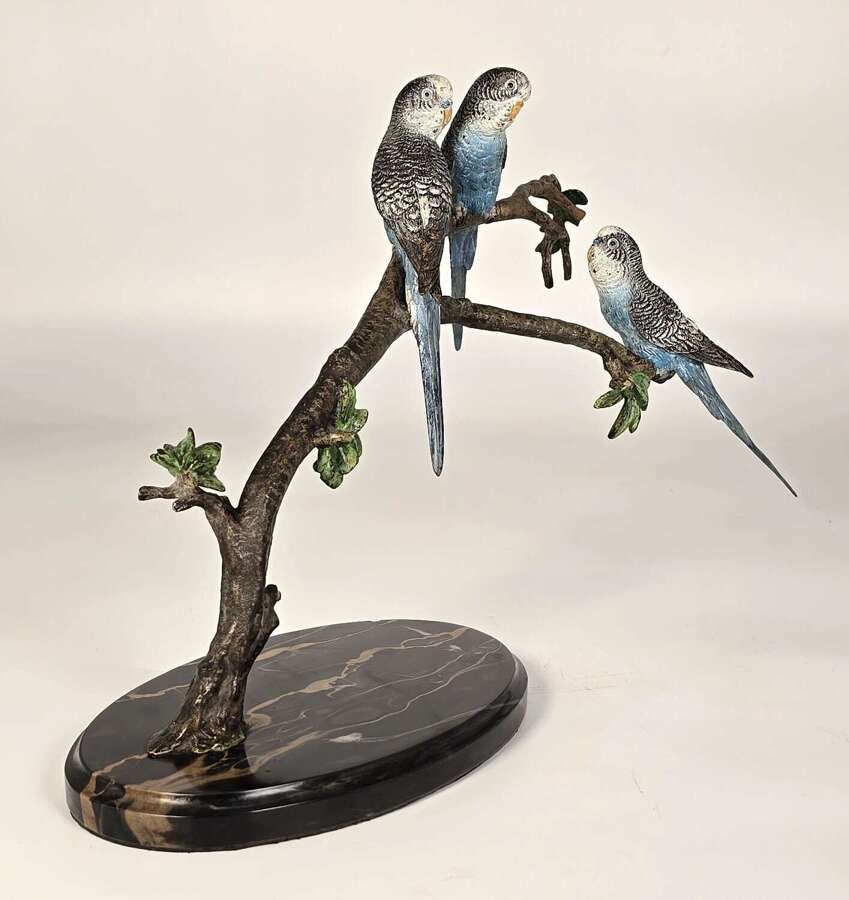 A large Austrian cold painted bronze study of three budgerigars perched on a leafy branch.